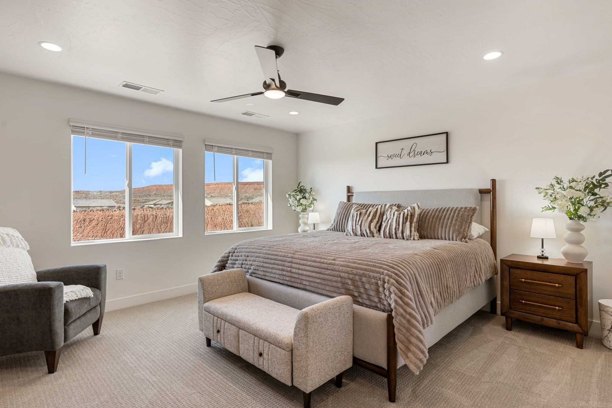 A bedroom with a bed, a chair, a bench, a nightstand, and a ceiling fan.