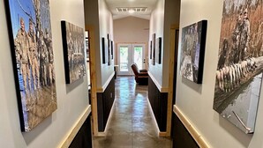 A hallway with framed photographs on the walls, a wooden bench, and a door at the end.