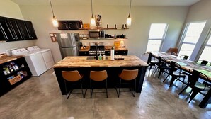 A kitchen with a central island, bar stools, a dining table with chairs, and a large window.