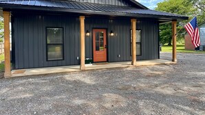 A building with a dark exterior, a wooden door, and a porch with columns.