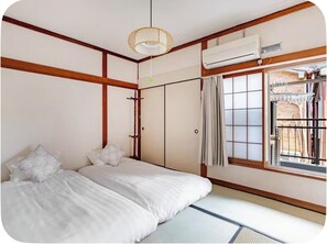 A traditional Japanese-style room with tatami flooring, a bed with white bedding, a shoji screen window, and an air conditioning unit. - 4 mins Metro to Namba. near stn. 2 floors japanese style.2tatami rooms, 2toilets (Bainan, Nishinari-ku, Osaka)