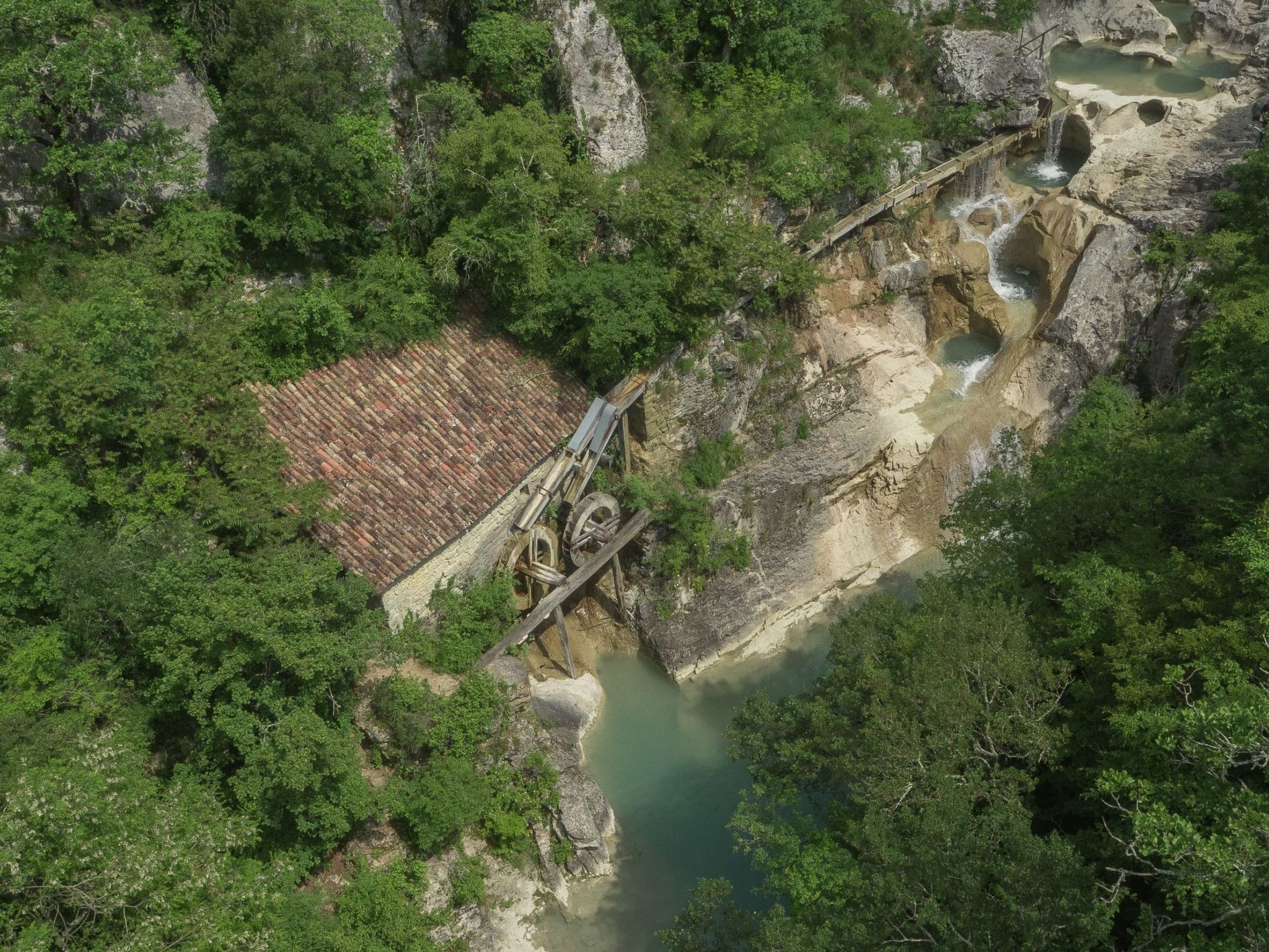 Vista aérea de un paisaje natural con un puente de madera, terreno rocoso y una pequeña masa de agua.