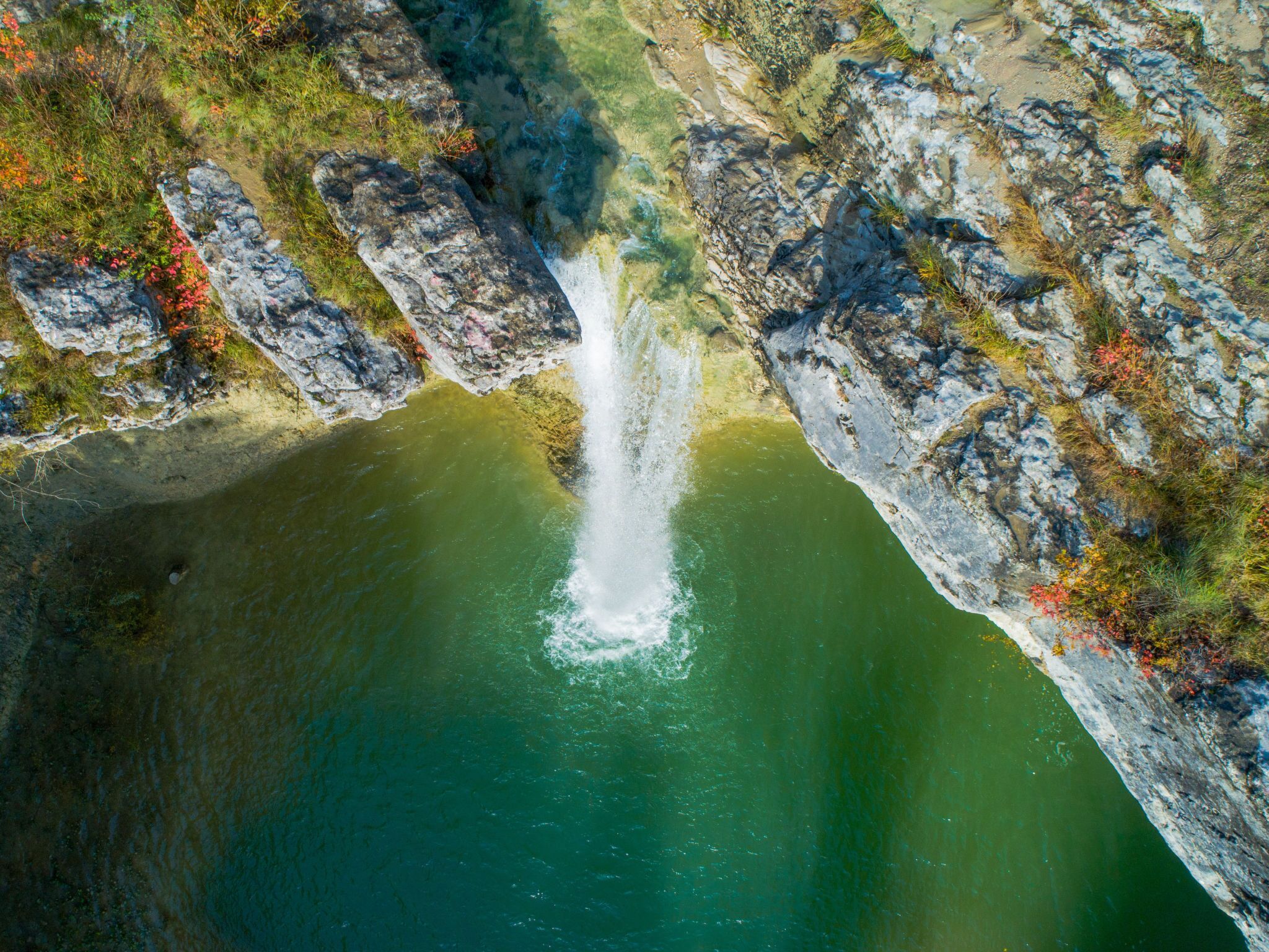 Eine Luftaufnahme eines Wasserfalls, der in einen Fluss stürzt, umgeben von felsigem Gelände.