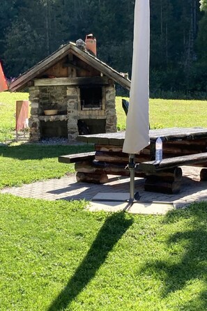 A stone building with a chimney, a picnic table, and a metal pole with a white cover. - Chalet Le Grandzon **** (bis 8 Personen) by Interhome (Champex)