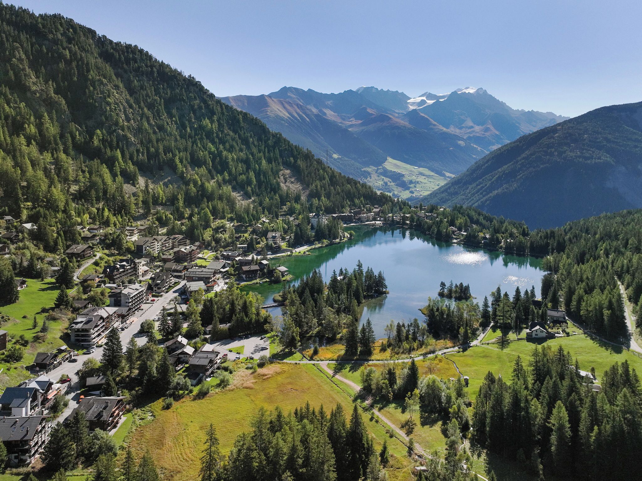 A mountainous area with a lake surrounded by forested hills. There are buildings near the lake, likely accommodations or facilities.