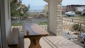 Ein Balkon mit Holztisch und Bank, mit Blick auf einen Yachthafen mit Booten und Gebäuden.
