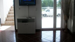 Ein Empfangsbereich mit Wand-Fernseher, einem weißen Konsolentisch und einer Fernbedienung sowie einer großen Schiebetür zu einem Parkplatz.