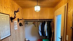 Een houten blokhut vanbinnen, met een bankje, kapstok en hanglamp.