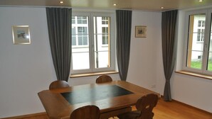 A dining area with a rectangular table and four chairs, large windows with curtains, and a wooden floor. - Blaues Haus by Interhome (Appenzell)