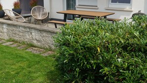 A patio with a wooden table and chairs, a stone wall, and a well-maintained hedge. - Bertsche 3 Schlafzimmer by Interhome (Rietheim)
