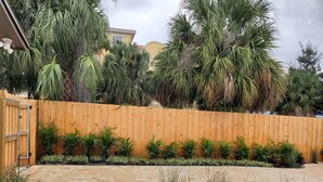 Un jardin avec une clôture en bois, diverses plantes et un chemin pavé.