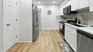 Une cuisine moderne avec des armoires blanches, un réfrigérateur en acier inoxydable, un four à micro-ondes et un revêtement mural décoratif.
