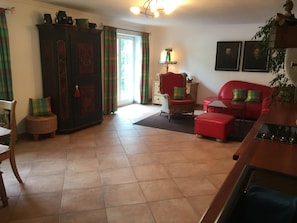 Un salon avec un canapé rouge, un fauteuil en osier, un buffet et une table à manger.