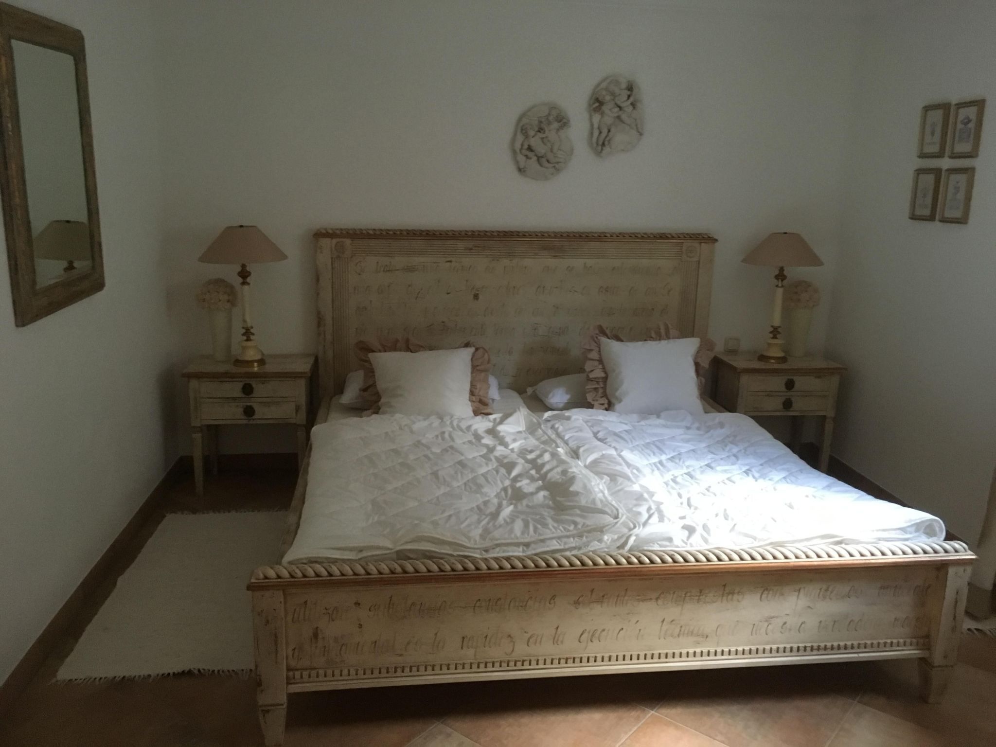A bedroom with a wooden bed, two bedside tables with lamps, and a mirror on the wall.