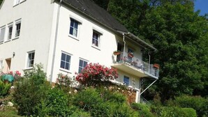 A white two-story house with a balcony, surrounded by lush greenery and a stone wall. - Tolle Wohnung in Klüsserath mit Großem Garten by Interhome (Klüsserath)