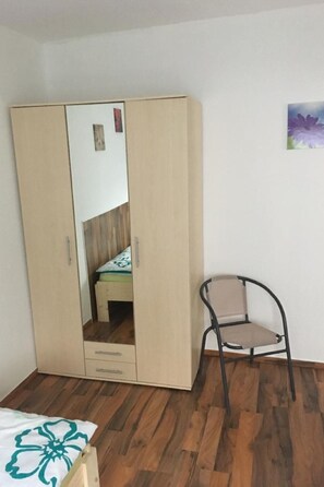 Ein Schlafzimmer mit einem hölzernen Kleiderschrank, einem Sessel und einem Bett mit floralem Überwurf.