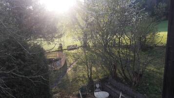 Ein Garten mit einer Terrasse, Metallstühlen und einem Tisch, umgeben von Bäumen und einem Holzzaun.