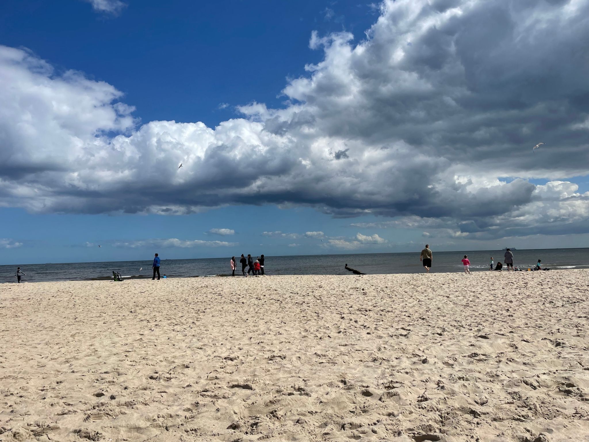 A sandy beach with people walking and standing, and a partly cloudy sky.