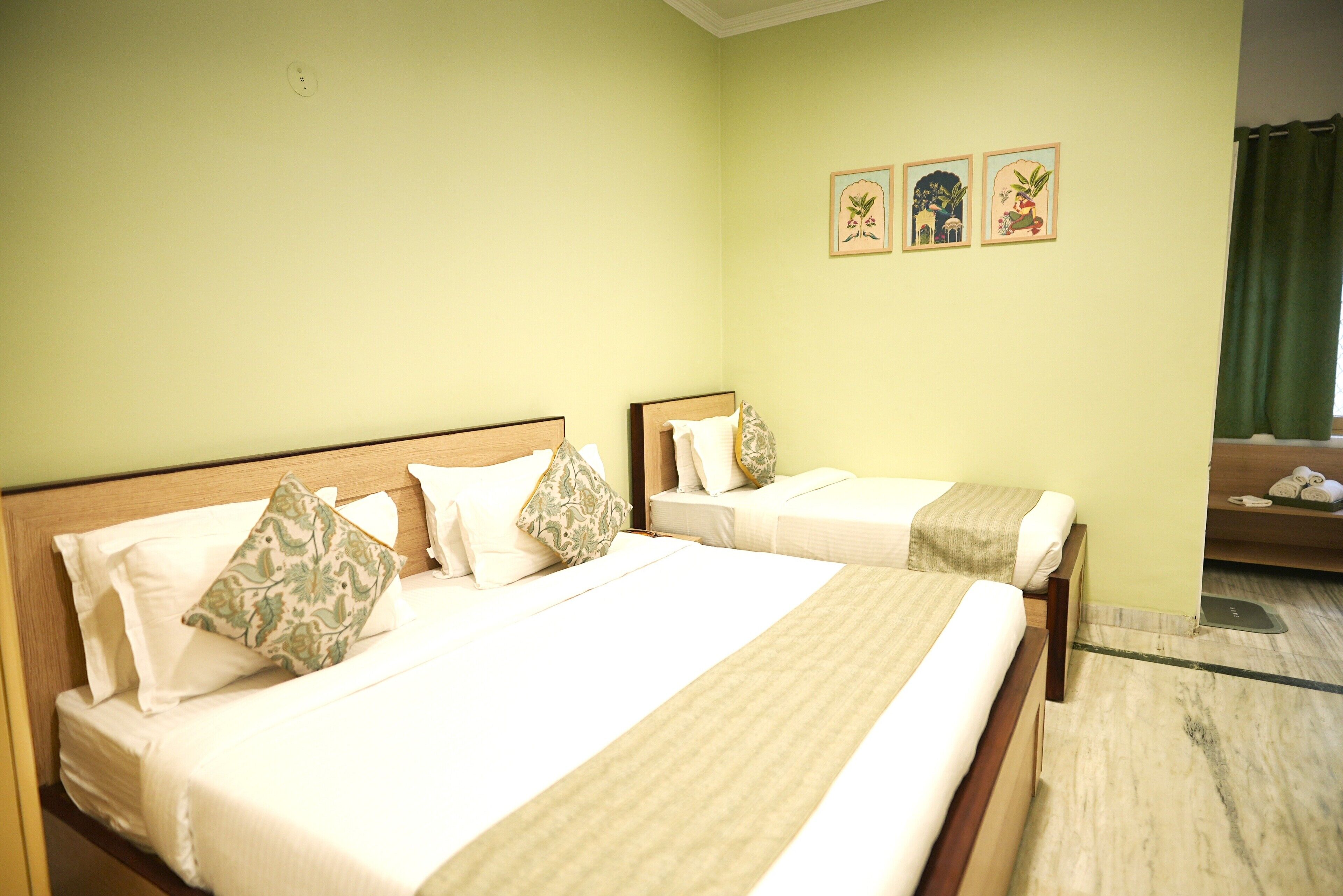 A hotel room with two beds, a green wall, and three framed pictures.
