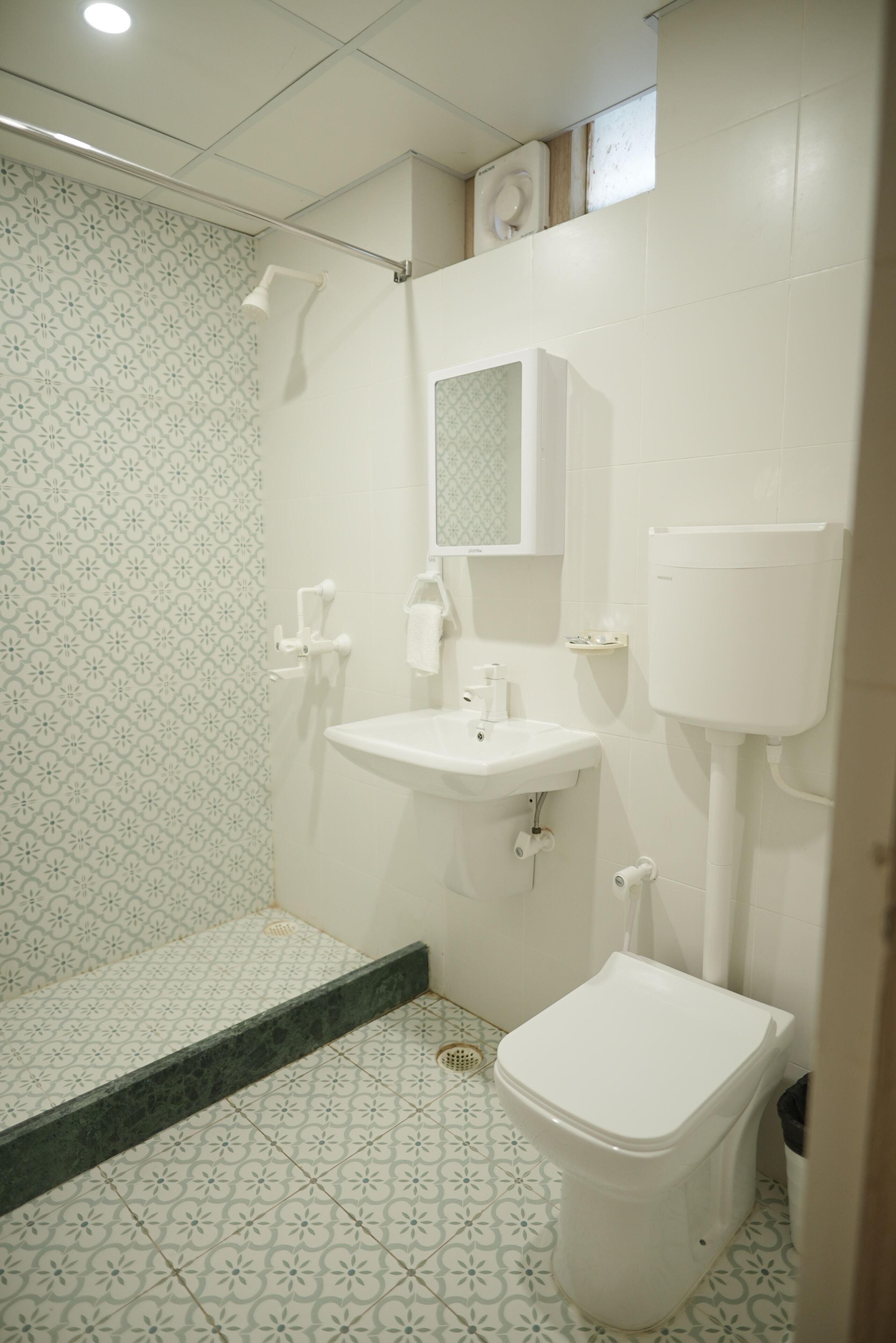 Un baño con ducha, lavabo, inodoro y azulejos estampados.