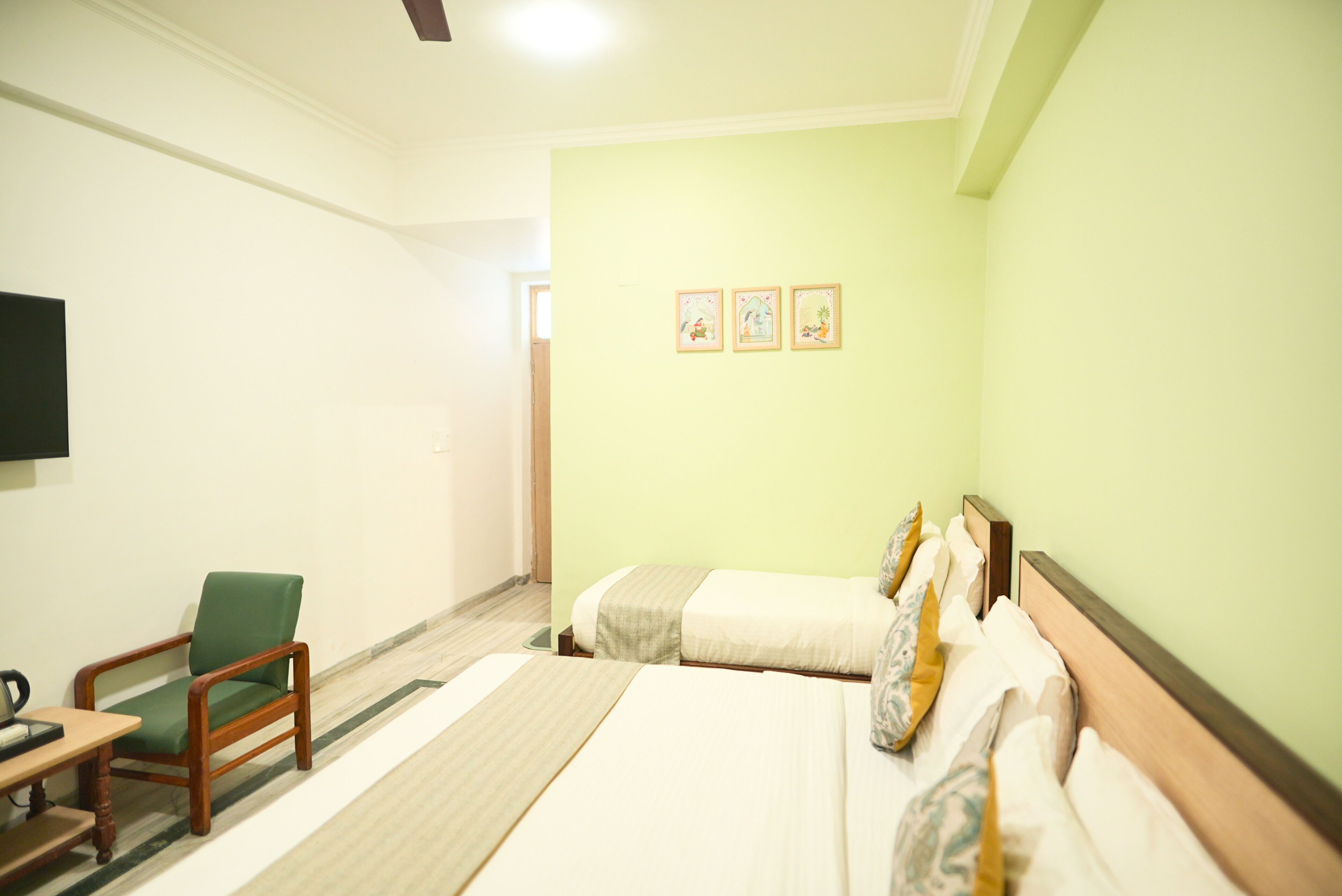 A hotel room with a bed, a chair, a flat-screen TV, and three framed pictures on the wall.