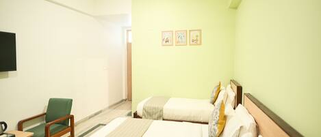 A hotel room with a bed, a chair, a flat-screen TV, and three framed pictures on the wall.