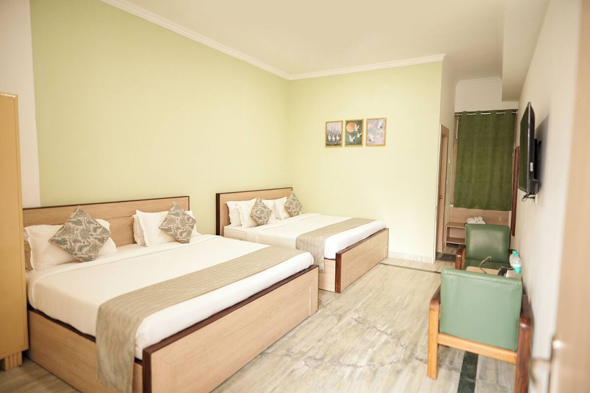 Une chambre d’hôtel avec deux lits, un fauteuil vert, un bureau et un téléviseur fixé au mur.