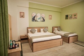 A hotel room with a large bed, a smaller bed, a nightstand, and a desk with a chair. There are three wall-mounted artworks depicting peacocks. - Shri Thakur Ji Niketan Near ISKCON  (Vrindavan)
