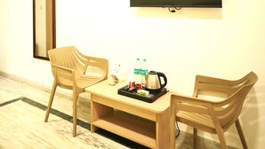 A room with a wooden table, two chairs, a flat-screen TV, a mirror, and a coffee maker. - Shri Thakur Ji Niketan Near ISKCON  (Vrindavan)