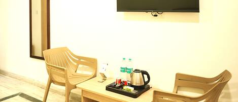 A room with a wooden table, two chairs, a flat-screen TV, a mirror, and a coffee maker.