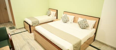 Habitación de hotel con dos camas individuales, una cama grande, cabecera de madera y pared verde.