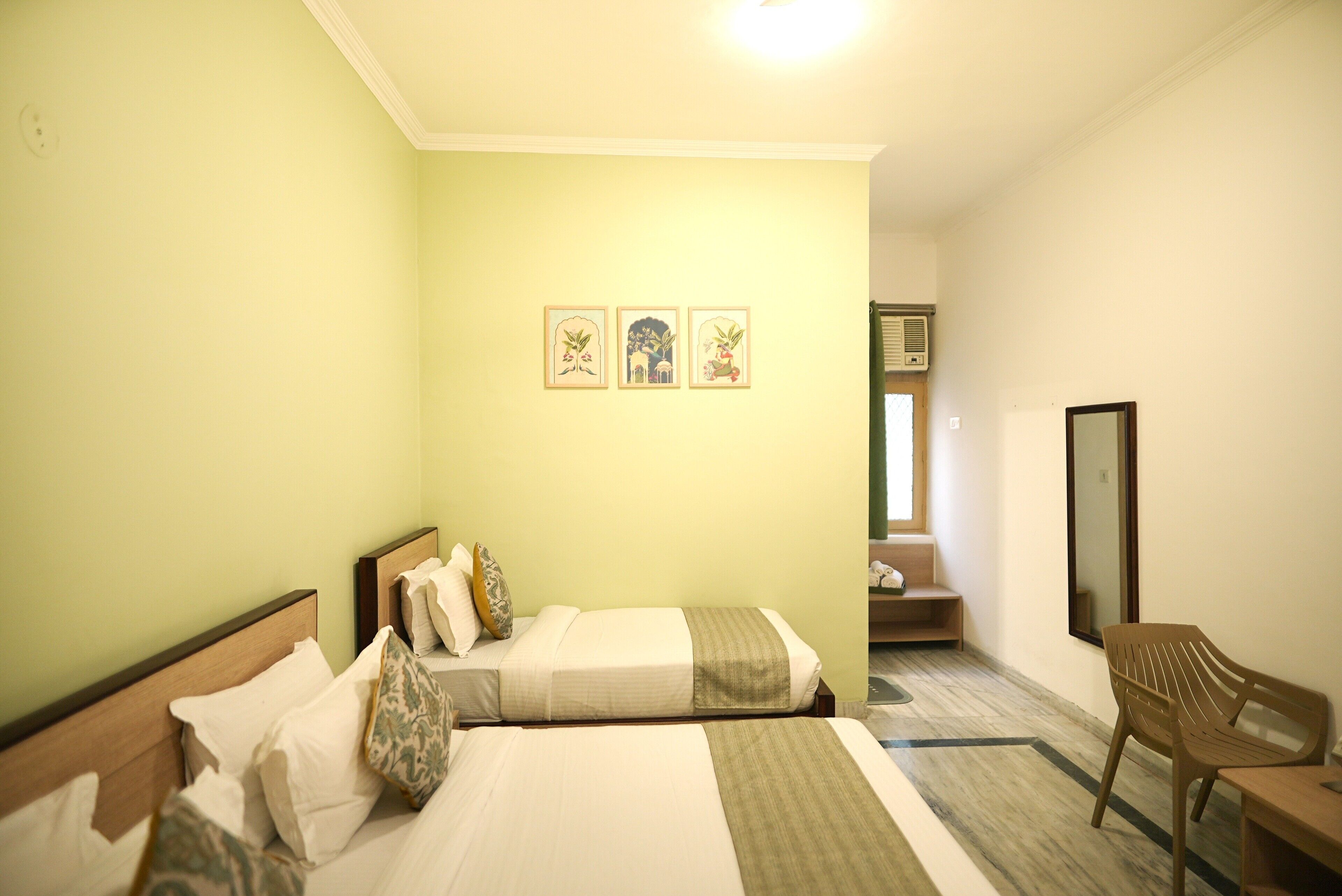 A hotel room with two beds, a chair, a small table, and a mirror.