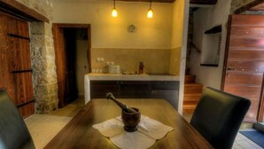 A rustic dining area with a wooden table, two chairs, a rustic mortar and pestle, and a kitchen in the background. - Istrien Traditionelles Steinhaus 3 by Interhome (Buzet)