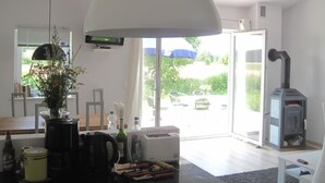 Ein modernes Wohnzimmer mit einer großen weißen Deckenleuchte, einem Kamin und Blick ins Freie durch eine Glastür.