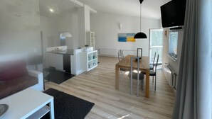 Eine moderne Küche mit weißen Schränken, ein Essbereich mit Holztisch und Stühlen sowie ein an der Wand montierter Fernseher.