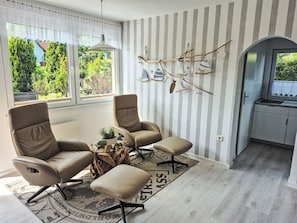 Ein modernes Wohnzimmer mit zwei Ledersesseln, einem kleinen Couchtisch und Blick ins Freie.