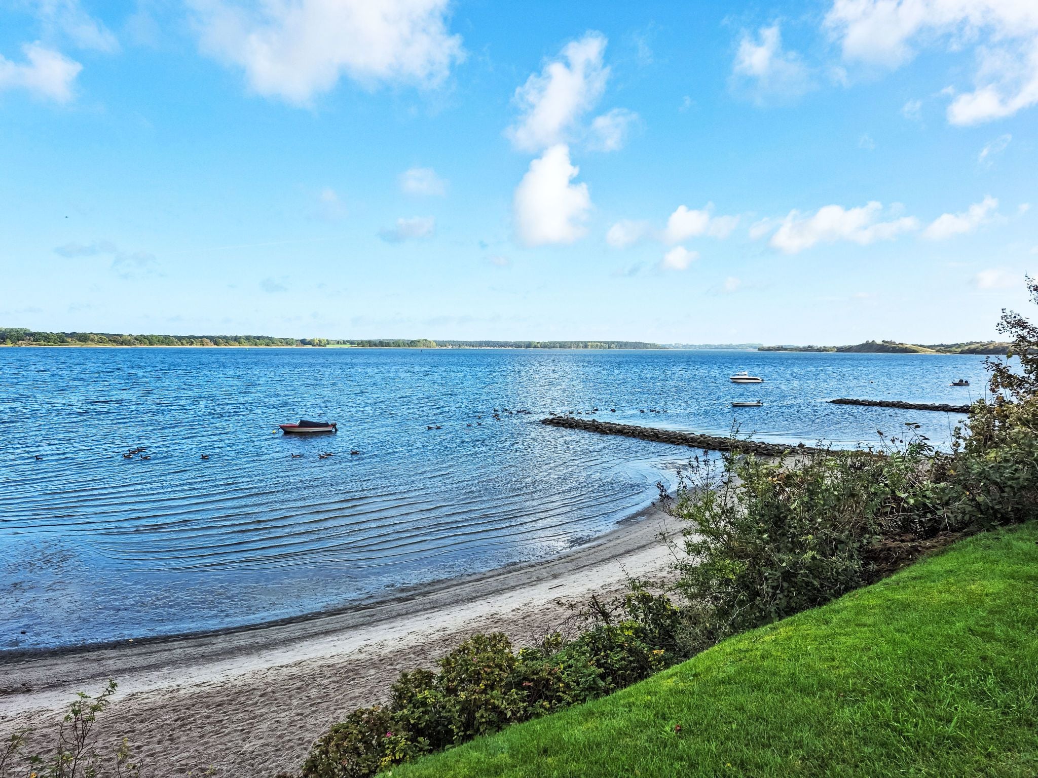A calm lake with boats, a sandy beach, and a grassy area.