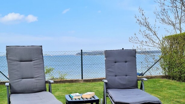 Two outdoor lounge chairs with cushions, a small table with books, and a chain-link fence in the background. - Ferienhaus direkt am Wasser by Interhome (Stralsund)