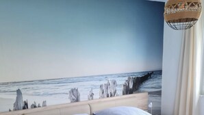 A bedroom with a bed, nightstand, and a wall mural of a beach scene. - Ferienhaus direkt am Wasser by Interhome (Stralsund)