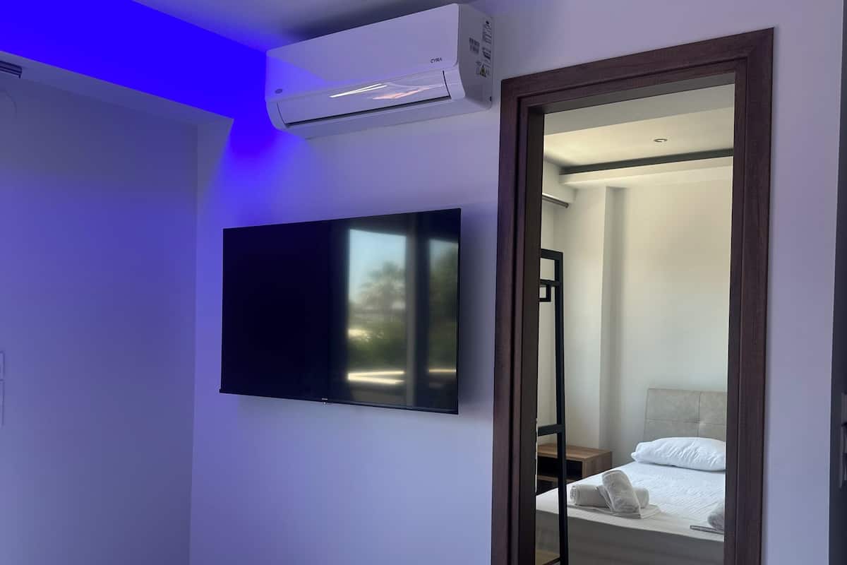 Une chambre d’hôtel avec un lit, un téléviseur fixé au mur, un appareil de climatisation et un miroir qui reflète une autre pièce.