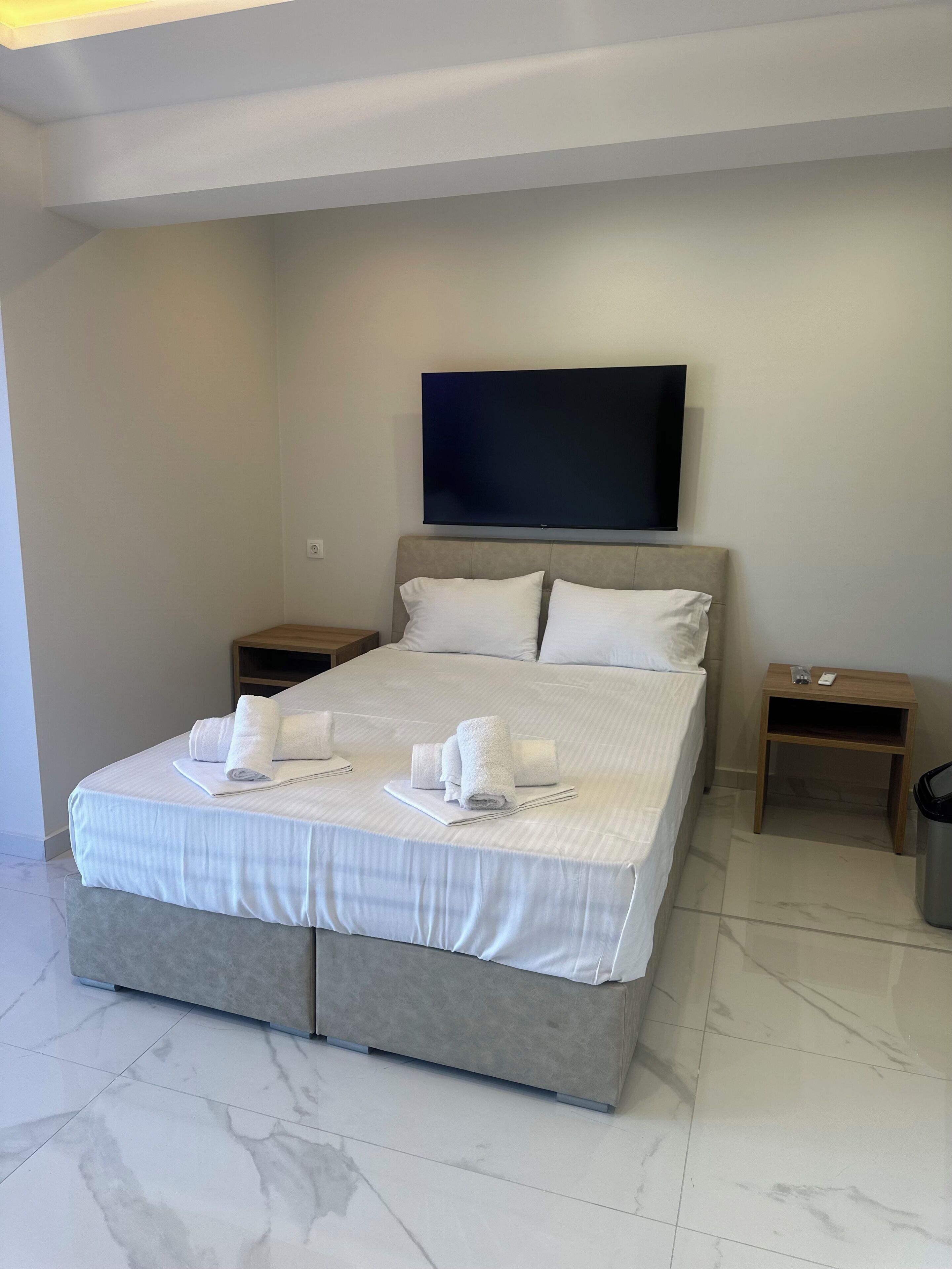 A hotel room with a large bed, a flat-screen TV mounted on the wall, two bedside tables, and a trash bin.