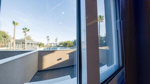 Vista a través de una ventana de una zona de piscina con palmeras y un edificio al fondo.