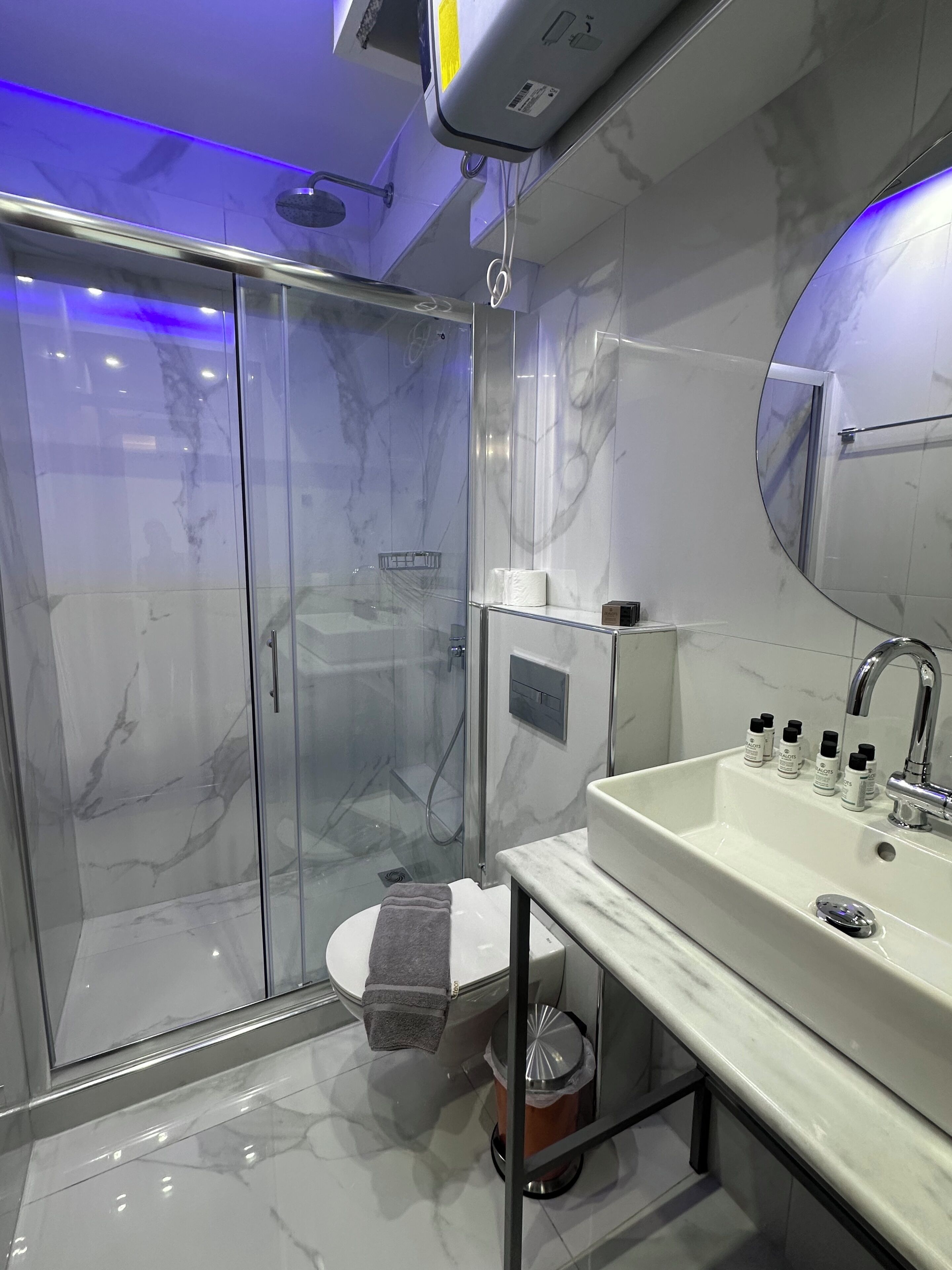 Een moderne badkamer met een douchecabine van glas, een wit wastafelmeubel met spiegel en een marmeren vloer.
