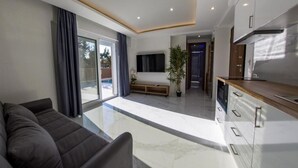 Una sala de estar moderna con un sofá, un televisor, una planta y una zona de cocina con encimera y armarios.