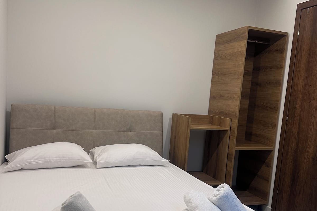 Un lit bien fait, avec du linge de lit blanc et des serviettes pliées, une armoire en bois et une tête de lit.