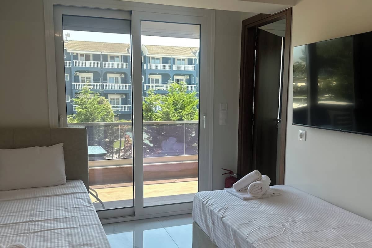 Une chambre d’hôtel avec deux lits, une télévision et un balcon offrant une vue sur les bâtiments et les arbres.