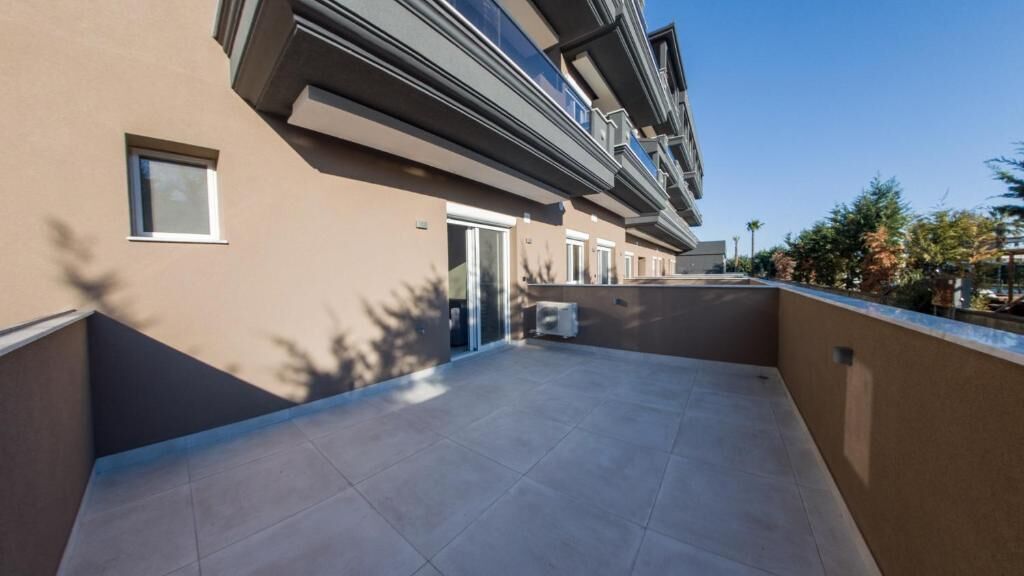 A modern apartment building with a flat roof terrace, a small window, and a door.