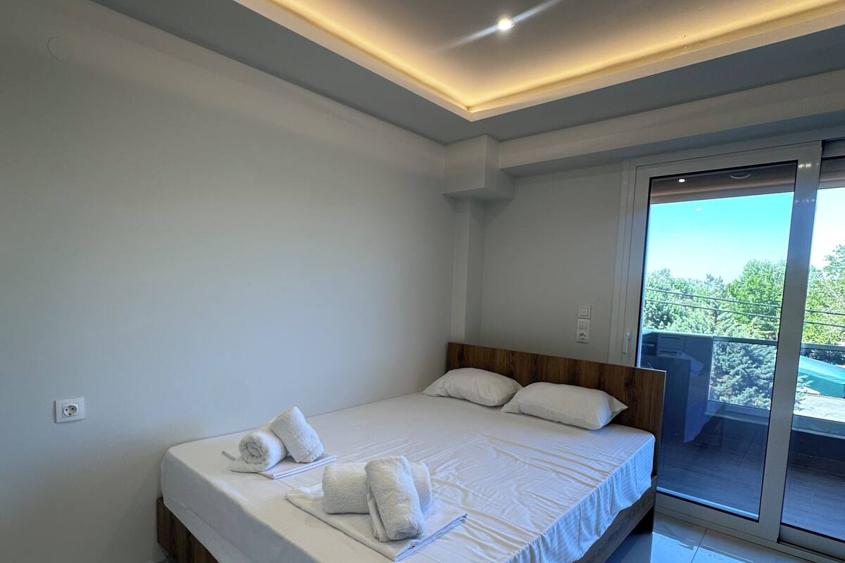 Une chambre moderne avec un grand lit, une tête de lit en bois et une porte en verre donnant sur un espace extérieur.