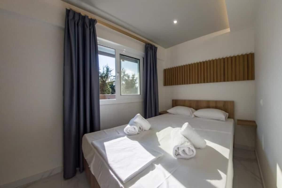Une chambre d’hôtel avec un lit, une fenêtre avec des rideaux et une tête de lit en bois.