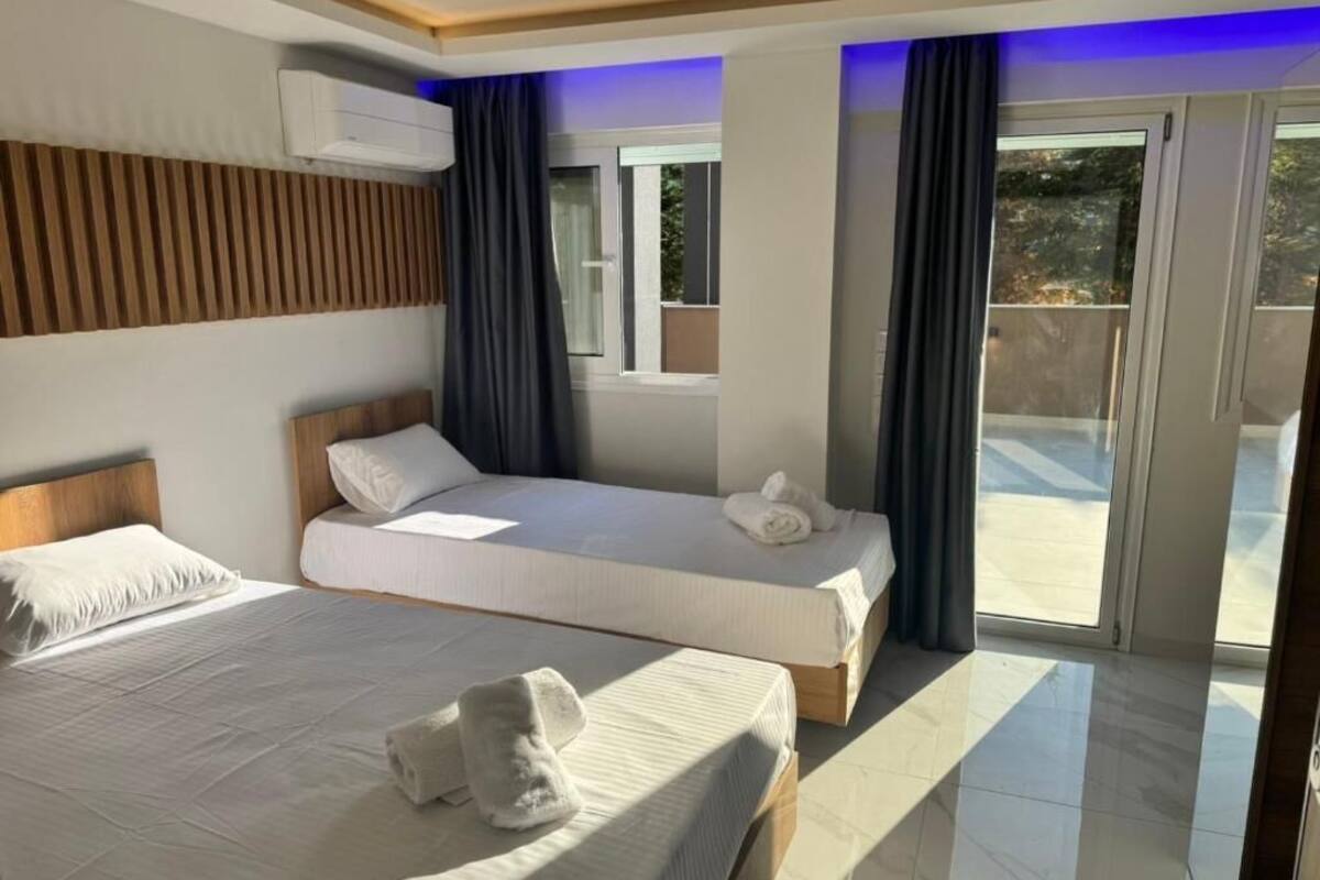 Une chambre d’hôtel avec deux lits, une tête de lit en bois, une grande fenêtre et un balcon.